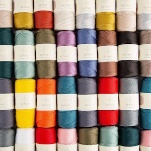 May include: A grid of colorful Sensy brand spools of thread. The spools are in various colors, including yellow, orange, red, blue, green, and purple. Each spool has a white label with the Sensy logo.