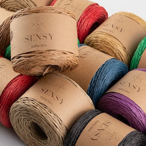 May include: A collection of colorful raffia yarn spools with the brand name "SENSY" printed on the labels. The spools are arranged in a circular pattern, with the brown spools in the center and the other colors surrounding them.