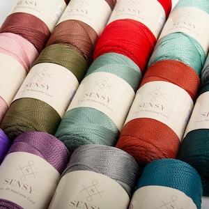 May include: A collection of colorful macrame cord spools in various shades, including red, green, and teal. Each spool is labeled with the brand name "SENSY" and product details. The image showcases a variety of colors and textures.