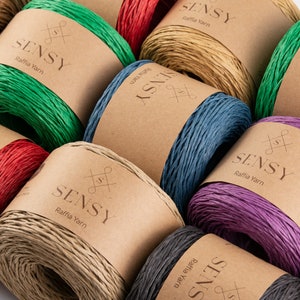 May include: Assortment of colorful raffia yarn spools with the brand name "SENSY" printed on each label. The yarn is available in green, red, beige, blue, purple, and black.