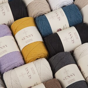May include: A close-up of various colors of 3 mm and 5 mm twisted macrame cord. The cord is made of cotton and is available in a variety of colors, including beige, white, black, gray, teal, yellow, and purple. The cord is labeled with the brand name "SENSY" and the size and type of cord.