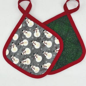 May include: Two red-trimmed pot holders. One is gray with a snowman pattern, the other is green with a sparkly texture.
