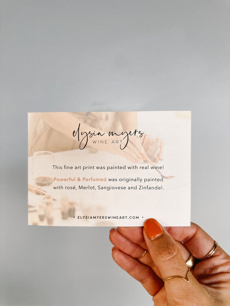 May include: A white card with the text "elysia myers, WINE ART" and the text "This fine art print was painted with real wine! Powerful & Perfumed was originally painted with ros&eacute;, Merlot, Sangiovese and Zinfandel. ELYSIAMYERSWINEART.COM."  The card is being held by a hand with orange nail polish.