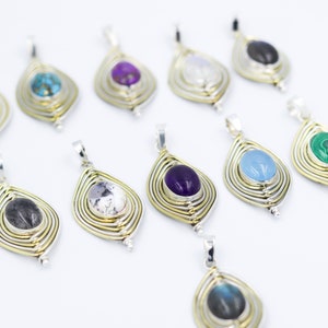 May include: A collection of 10 silver and gold pendants featuring different coloured gemstones. Each pendant has a teardrop shape with a gemstone in the centre and multiple gold rings around it.