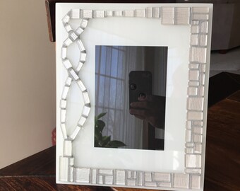 Classic white glass picture frame with beveled edge.  Enhanced with white glass mosaic tiles and silver grout. Holds 5x7 pic.