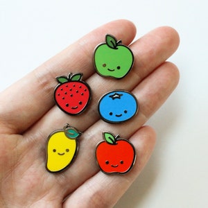 Peut inclure: Cinq épingles en émail représentant des fruits et une myrtille en dessin animé. Les épingles sont vertes, rouges, jaunes, bleues et rouges. Chaque épingle a un visage souriant.