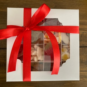 May include: A white gift box with a red ribbon tied around it. The box has a clear window on the front, revealing a variety of colorful gummy candies inside.