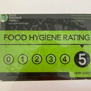 May include: A green and black food hygiene rating sticker with a white background. The sticker has a rating of 5, which is very good. The sticker is from the Food Standards Agency.