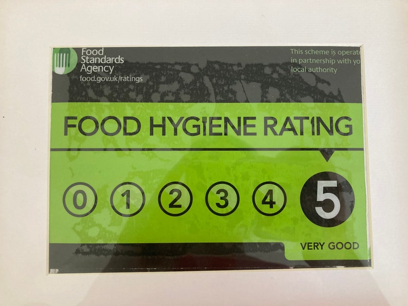 May include: A green and black food hygiene rating sticker with a white background. The sticker has a rating of 5, which is very good. The sticker is from the Food Standards Agency.