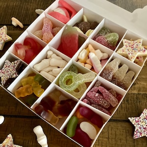 May include: A white box filled with assorted candies. The candies are in individual compartments and include gummy candies, jelly beans, and chocolate candies.
