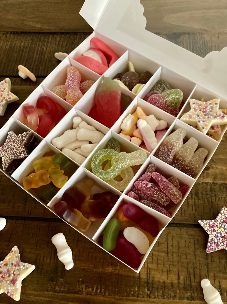 May include: A white box filled with assorted candies. The candies are in individual compartments and include gummy candies, jelly beans, and chocolate candies.