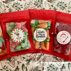May include: Five red cellophane bags filled with colourful sweets. Each bag has a circular sticker with festive designs and text, including "Magic Elf Beans," "Elf Walking Sticks," and "Carrots for the Reindeer."