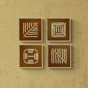 Op de afbeelding: Vier vierkante ingelijste prints met bruine achtergronden en witte geometrische ontwerpen. De ontwerpen zijn abstract en bevatten lijnen en vormen.