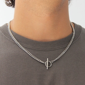 May include: A silver chain necklace with a toggle clasp. The chain is a curb style and is worn by a person.
