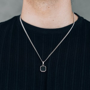 May include: A silver chain necklace with a black square pendant.