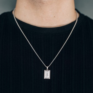 May include: A silver chain necklace with a rectangular pendant featuring a geometric design.