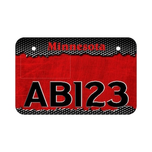 May include: A red metal license plate with a black metal grid pattern and the word "Minnesota" in red text. The license plate number is "ABI23" in black text.