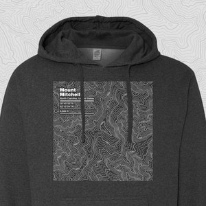 May include: Dark gray hooded sweatshirt featuring a white topographic map of Mount Mitchell in North Carolina. The text "Mount Mitchell" is displayed above the map, along with coordinates and elevation of 6,684 ft.
