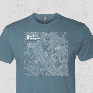 May include: A blue t-shirt with a white topographic map design of Mount Timpanogos in Utah, United States. The map includes the coordinates 40°23′27″N 111'38'45"W and the elevation 11,753 ft.