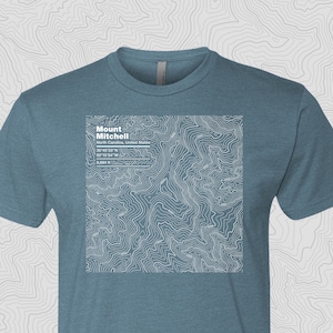 May include: A teal blue t-shirt with a white topographic map design of Mount Mitchell, North Carolina, United States. The map includes the coordinates 35°45′53″N and 82°15'54"W.