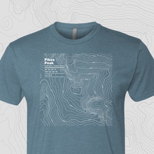 May include: A blue t-shirt with a white topographic map design of Pikes Peak, Colorado. The map includes the peak's elevation, latitude, and longitude.