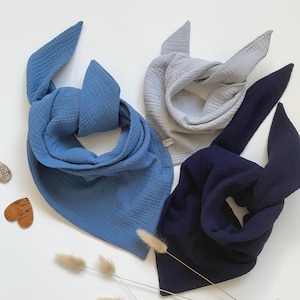 Könnte beinhalten: Drei Baby-Bandana-Lätzchen aus Baumwollmusselin in Blau, Grau und Dunkelblau. Die Lätzchen sind dreieckig gefaltet und aus einem weichen, atmungsaktiven Stoff gefertigt.