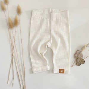 May include: White waffle knit baby leggings with a brown elephant logo patch on the right leg.