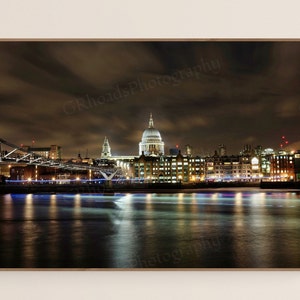 Puede incluir: Una vista nocturna del horizonte de la ciudad con la Catedral de San Pablo iluminada en la distancia. El Puente del Milenio está en primer plano, con el río Támesis reflejando las luces de la ciudad.