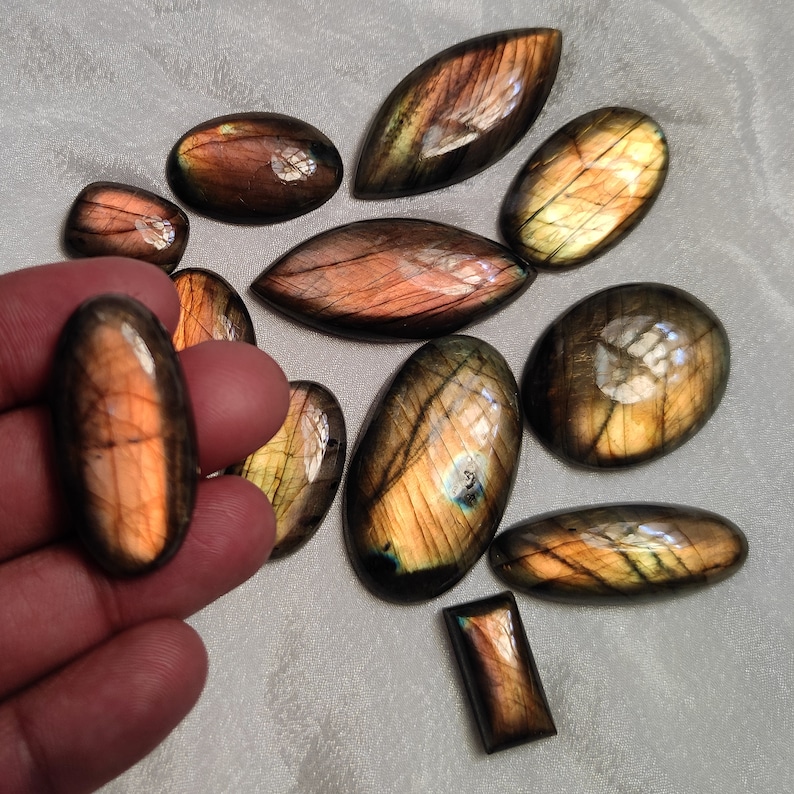 May include: A collection of 11 labradorite gemstone cabochons in various shapes and sizes. The stones are a mix of brown, gold, and green with iridescent flashes.