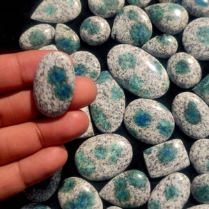 May include: A collection of polished, oval-shaped, blue and white speckled stones. The stones have a mottled appearance with a white base and blue speckles.