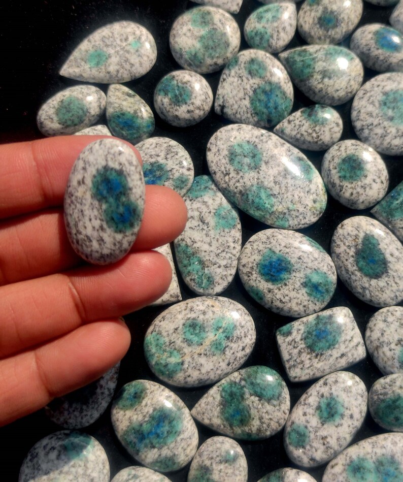 May include: A collection of polished, oval-shaped, blue and white speckled stones. The stones have a mottled appearance with a white base and blue speckles.