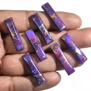 K&ouml;nnte beinhalten: Sieben rechteckige Cabochons aus violettem und goldenem Edelstein. Die Steine haben ein marmoriertes Muster mit goldenen Flocken.