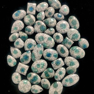 May include: A collection of 40+ polished, white and green, speckled, oval and teardrop shaped gemstones with blue flecks.