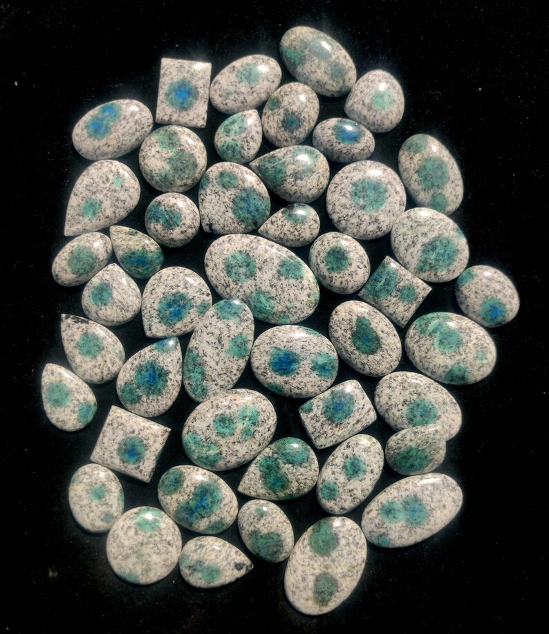 May include: A collection of 40+ polished, white and green, speckled, oval and teardrop shaped gemstones with blue flecks.