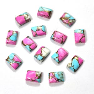 May include: A collection of rectangular gemstone cabochons. The stones feature a vibrant pink base color, accented with patches of turquoise, white, and gold veining. The gemstones are arranged on a white surface.