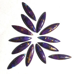 May include: A collection of 12 purple and gold cabochons arranged in a starburst pattern. The cabochons are oval shaped and have a marbled appearance.