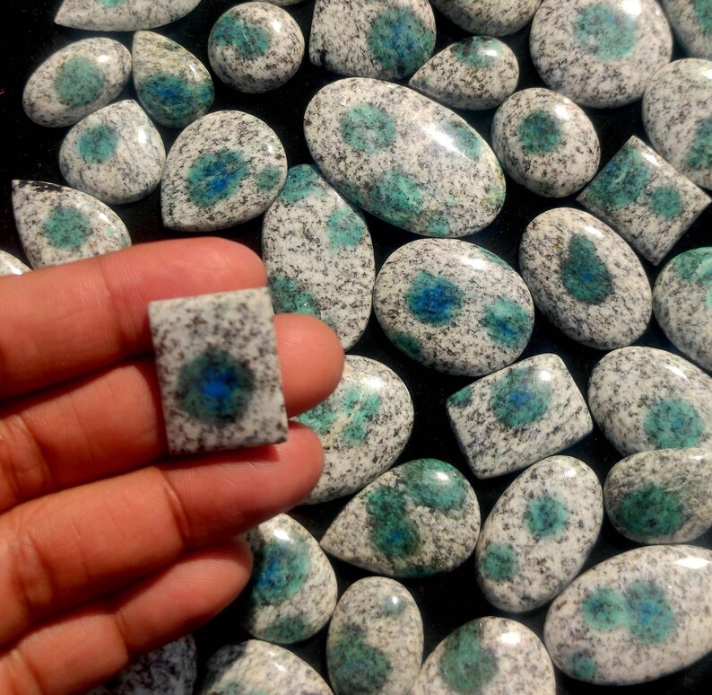 May include: A collection of polished, oval-shaped, and teardrop-shaped stones with a white and blue speckled pattern. The stones are displayed on a black surface.