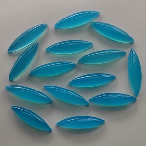 Puede incluir: Una colecci&oacute;n de 15 cabujones ovalados de color azul turquesa, dispuestos en un patr&oacute;n circular sobre una superficie blanca.