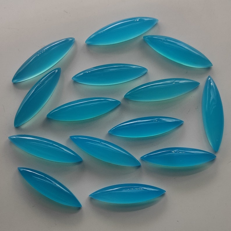 Puede incluir: Una colecci&oacute;n de 15 cabujones ovalados de color azul turquesa, dispuestos en un patr&oacute;n circular sobre una superficie blanca.