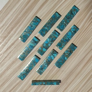 May include: Ten turquoise and gold rectangular pieces of material, arranged in a pattern on a wooden surface. A smaller piece of the same material is in the bottom centre of the image.