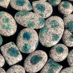 May include: A collection of polished, oval-shaped, blue and white speckled stones. The stones have a mottled appearance with blue and white speckles.