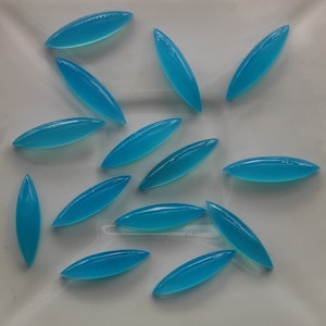 Puede incluir: Una colecci&oacute;n de 15 cabujones de piedra preciosa azul turquesa, cada uno con forma de &oacute;valo largo, dispuestos sobre una superficie blanca.