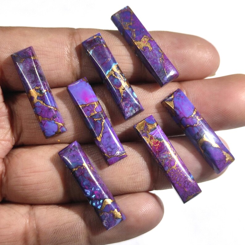 K&ouml;nnte beinhalten: Sieben rechteckige Cabochons aus violettem und goldenem Edelstein. Die Steine haben ein marmoriertes Muster mit goldenen Flocken.