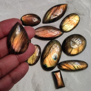 May include: A collection of ten labradorite gemstone cabochons in various shapes and sizes. The stones are a mix of brown, gold, and green with iridescent flashes.