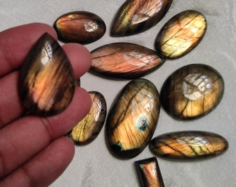 May include: A collection of ten labradorite gemstone cabochons in various shapes and sizes. The stones are a mix of brown, gold, and green with iridescent flashes.