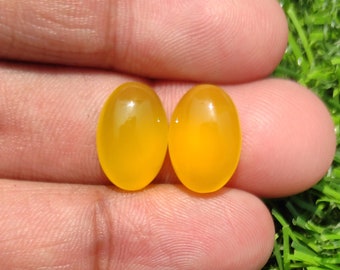 May include: Two oval-shaped yellow gemstones, likely citrine, are shown in a hand. The stones are smooth and polished, with a slight sheen.