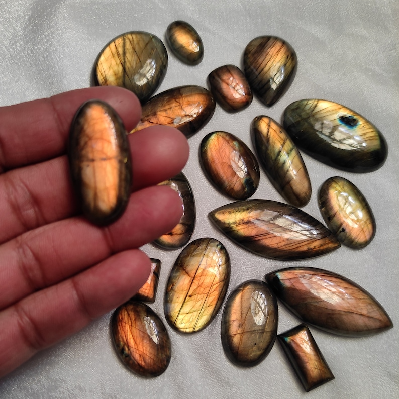 May include: A collection of 15 labradorite gemstone cabochons in various shapes and sizes. The stones are a mix of brown, gold, and green with iridescent flashes.
