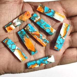 May include: A collection of eight turquoise, orange, and white cabochons. The cabochons are rectangular in shape and have a smooth, polished finish.