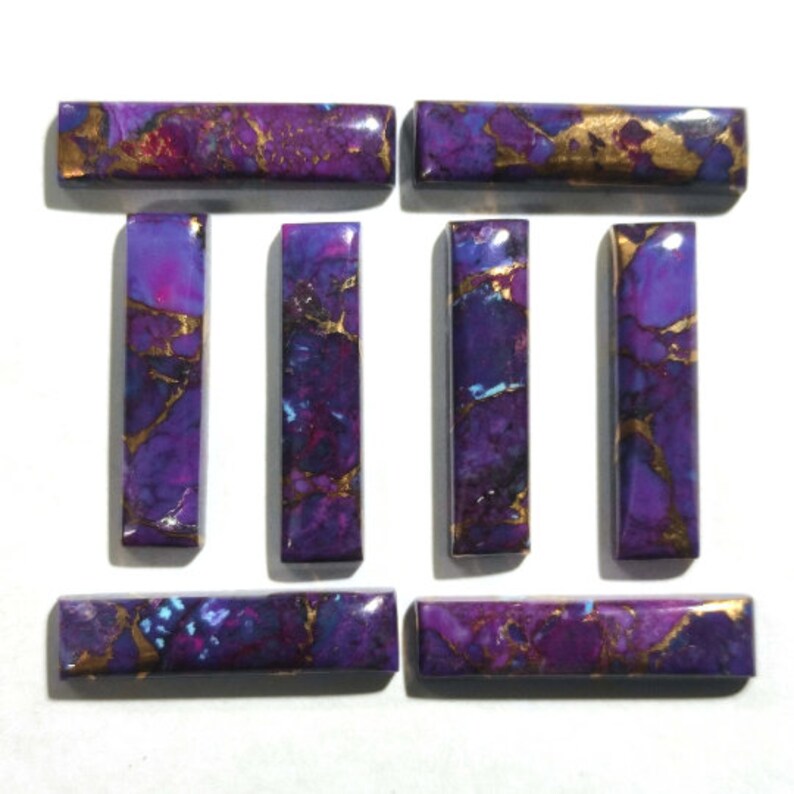 K&ouml;nnte beinhalten: Satz von zehn violetten und goldenen Cabochons, jeder mit einem einzigartigen Muster aus wirbelnden Farben und goldenen Flocken. Die Cabochons sind rechteckig und haben eine glatte, polierte Oberfl&auml;che.