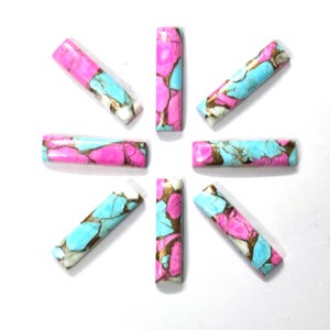 May include: Eight rectangular gemstone beads arranged in a circular pattern. The beads feature a mix of pink, turquoise, white, and gold colors. The gemstones are polished and have a marbled appearance, with a glossy finish.